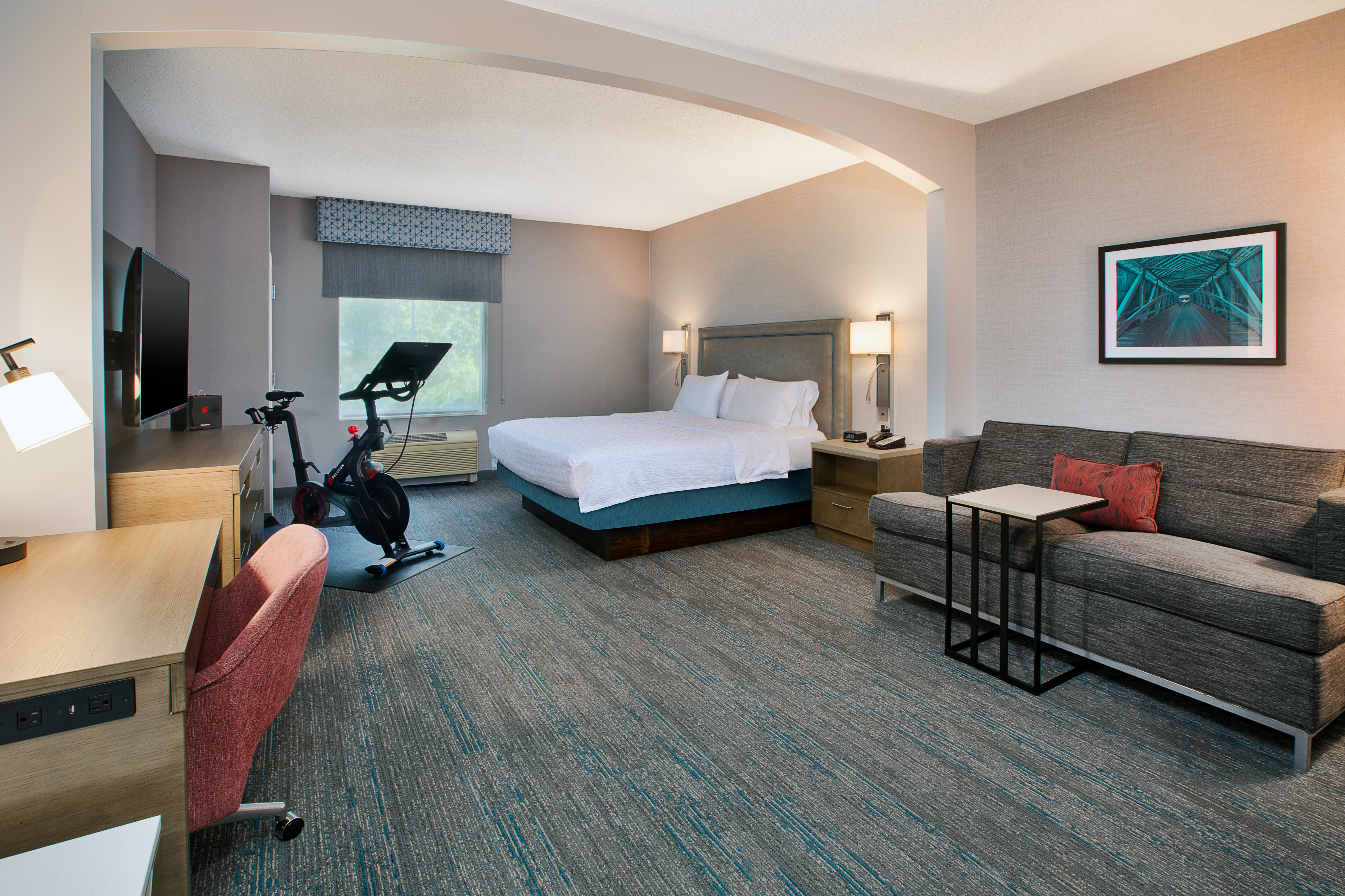 Peloton guest room with one king bed, work desk, TV, and a Peloton bike.