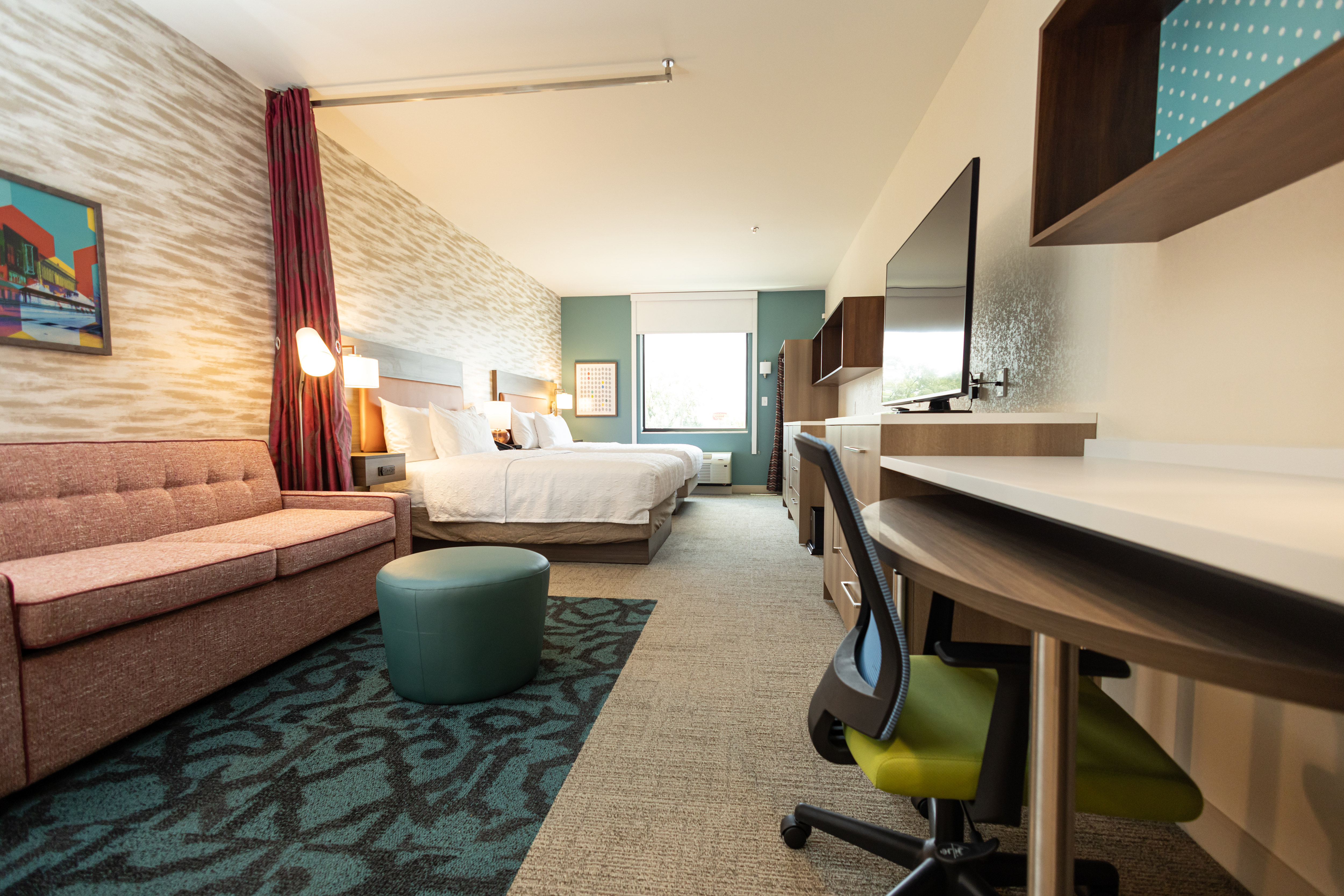 Suite lounge area with sofa, TV, work desk and two beds.
