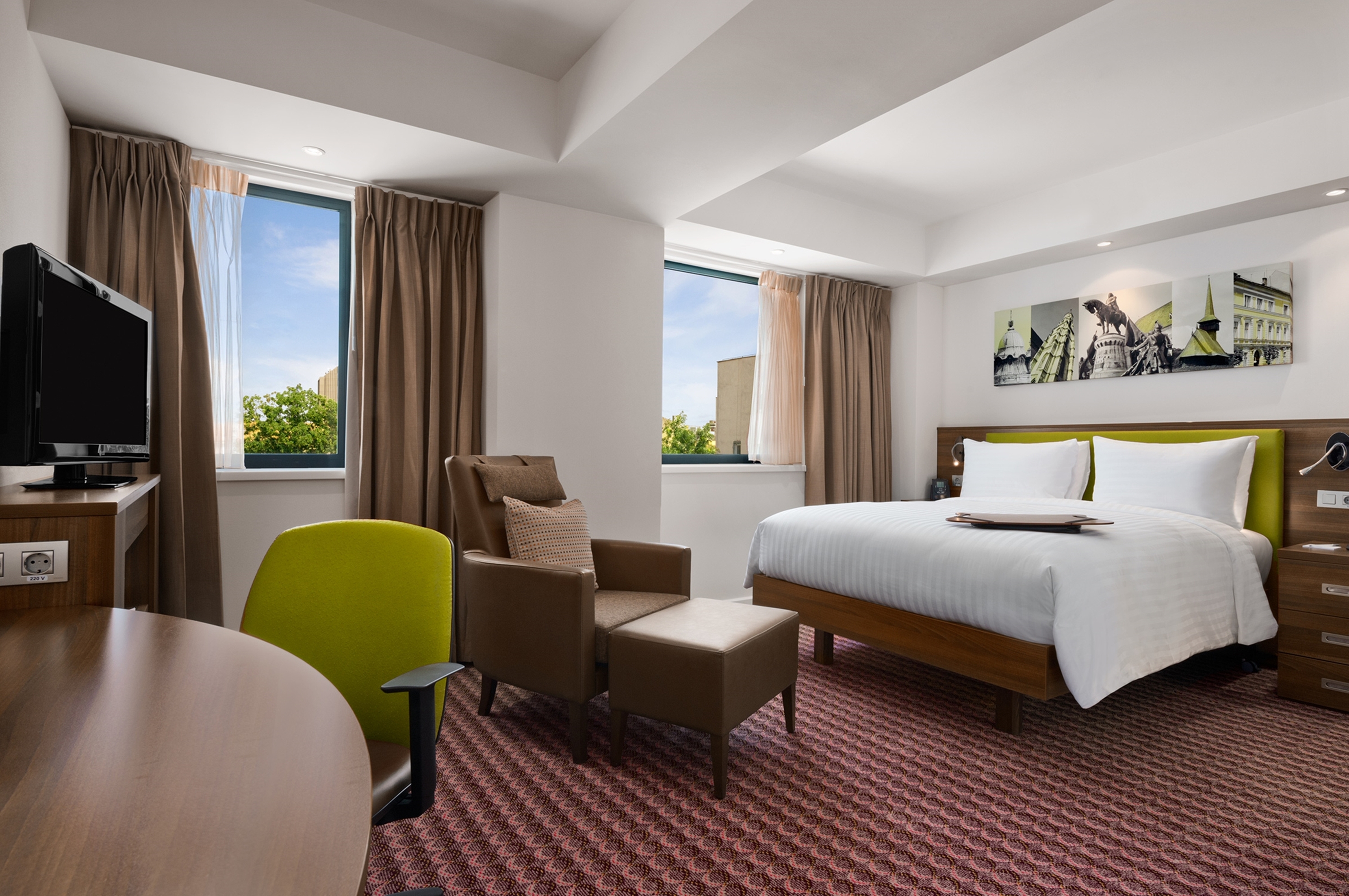 HDTV and Bed in Guest Room with Armchair Desk and Large Windows