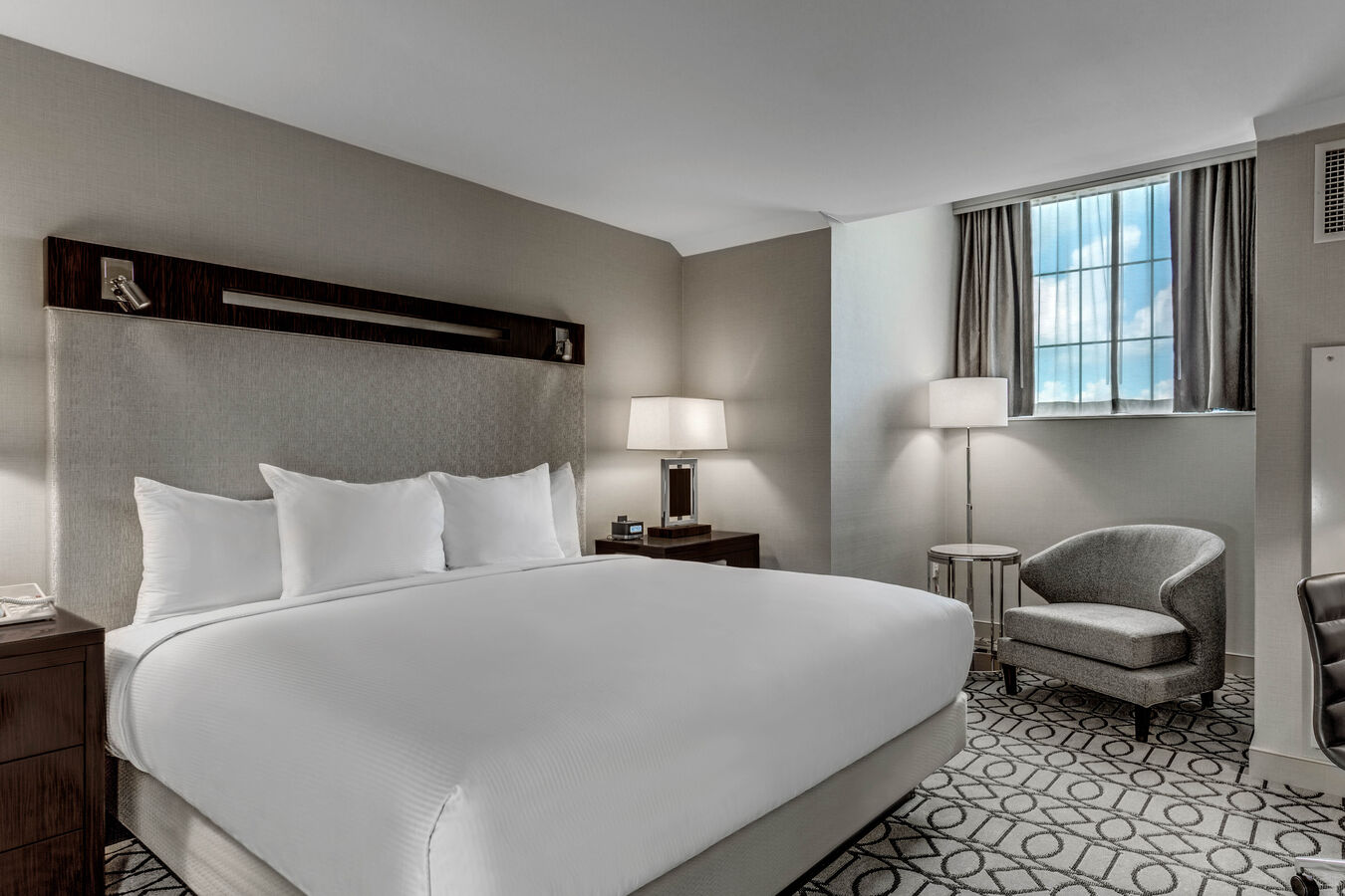 King Bed and Bedside Tables Facing Work Desk with Reading Chair and Lamp Under Window