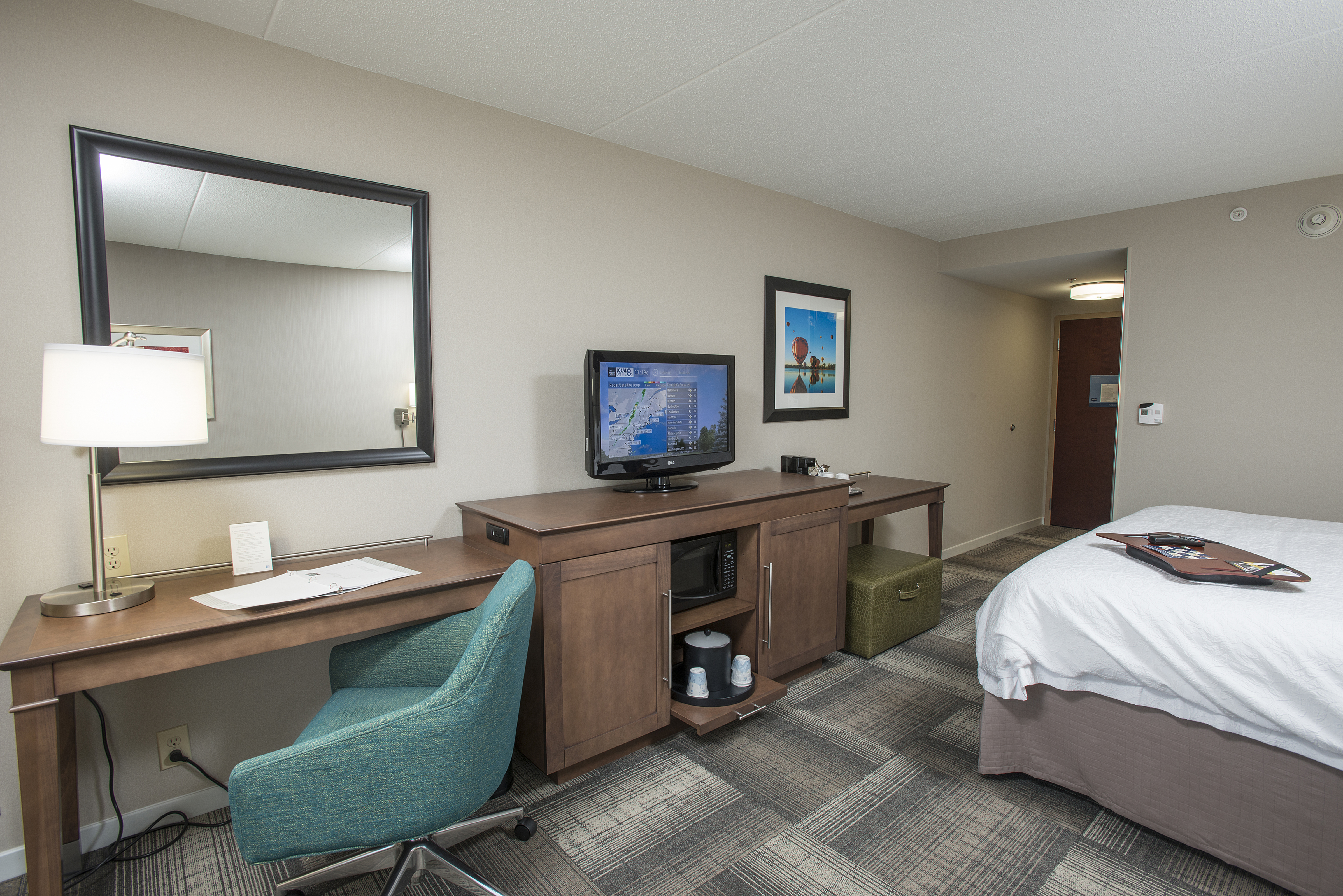 King Bed Facing TV and Work Desk With Chair. Mirror, Wall Art, and View of Entry