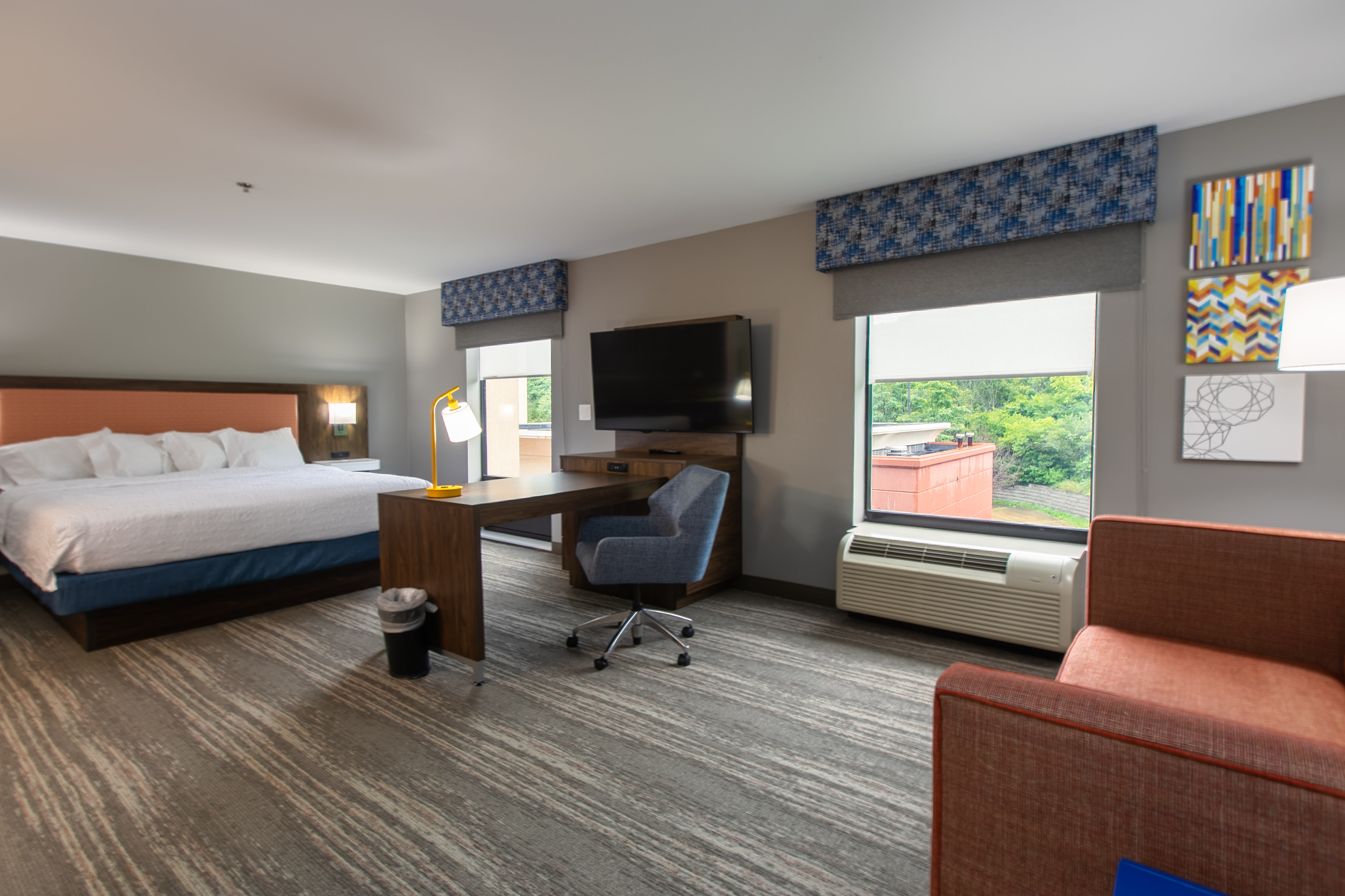 Guest room with a single bed, nightstands, a work desk, and a wall-mounted TV near large windows.