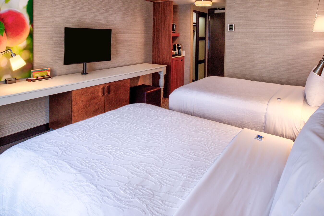 Two Double Beds Facing Colorful Wall Art by TV, and View of Entry
