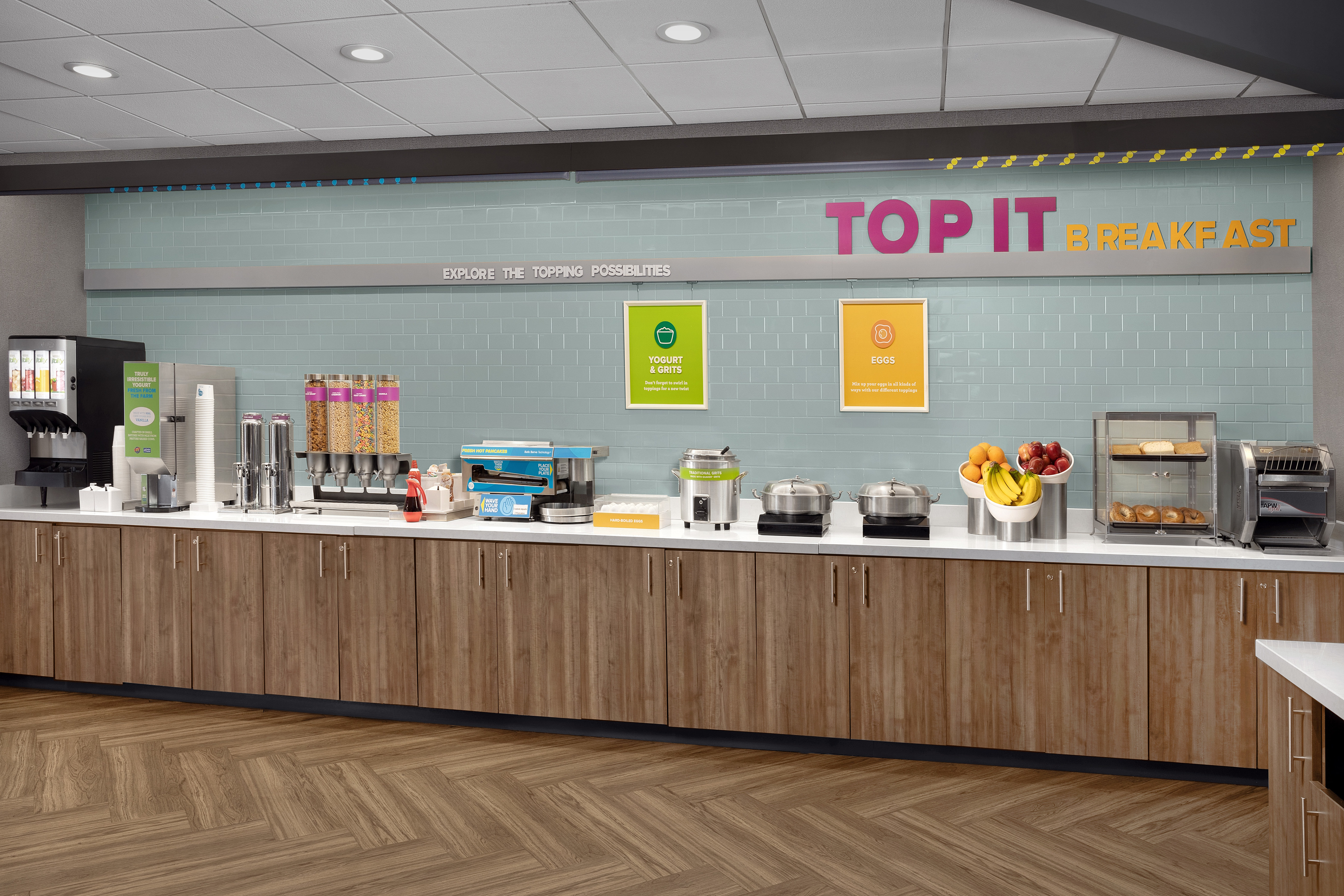 Breakfast buffet set-up with juices, hot drinks, cereal bar, pancake machine, yoghurt, grits, eggs, fruit and bread selection including bagels.