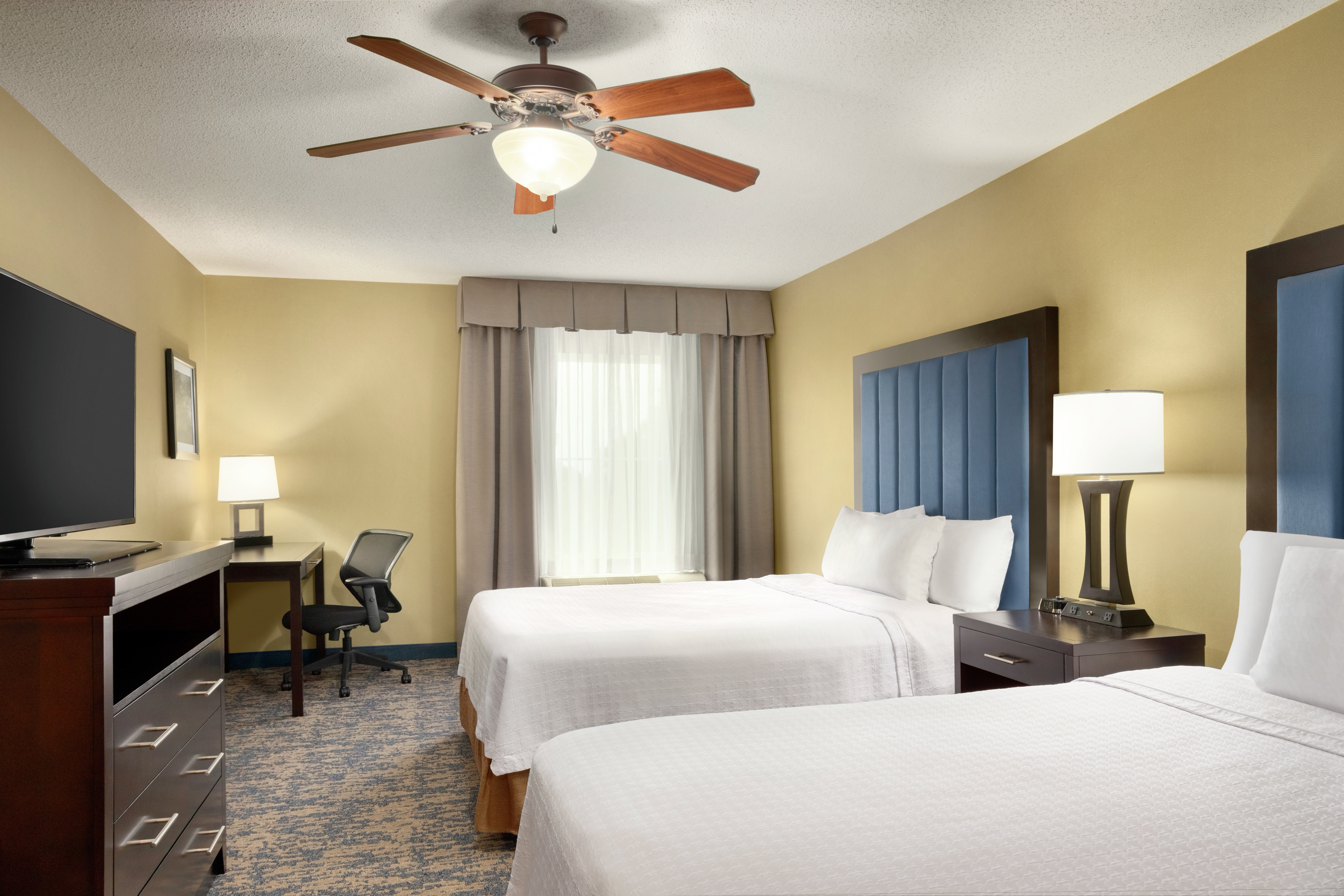 Private bedroom in suite featuring a TV, work desk, and two comfortable queen beds.