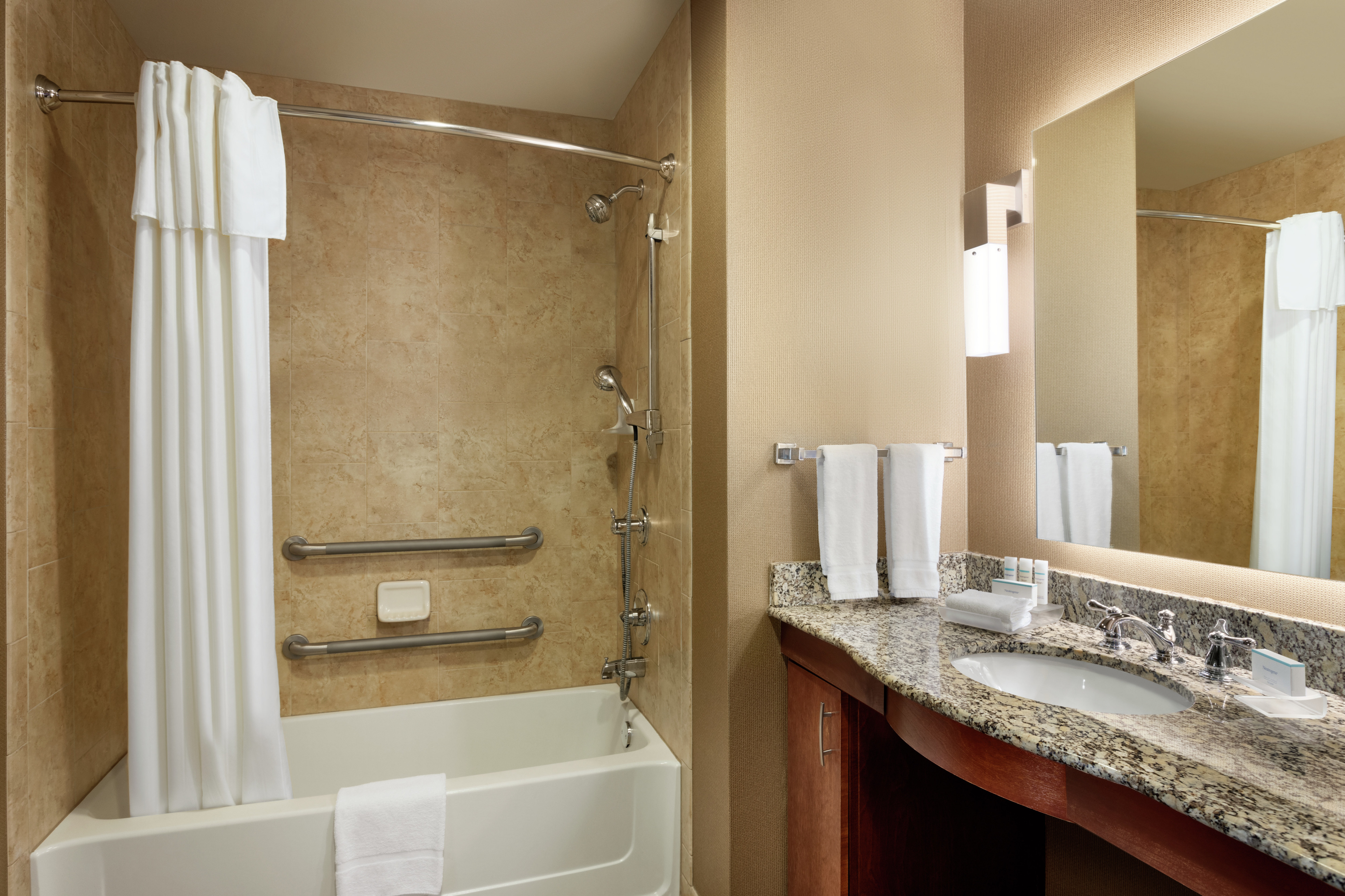 Bright accessible bathroom featuring tub with grab bars, large vanity, and mirror.
