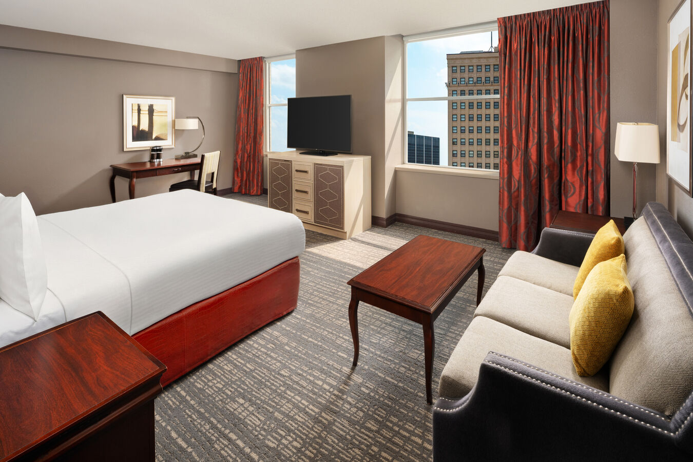 Executive suite bedroom with one bed, a TV, sofa and a large window with a city view.