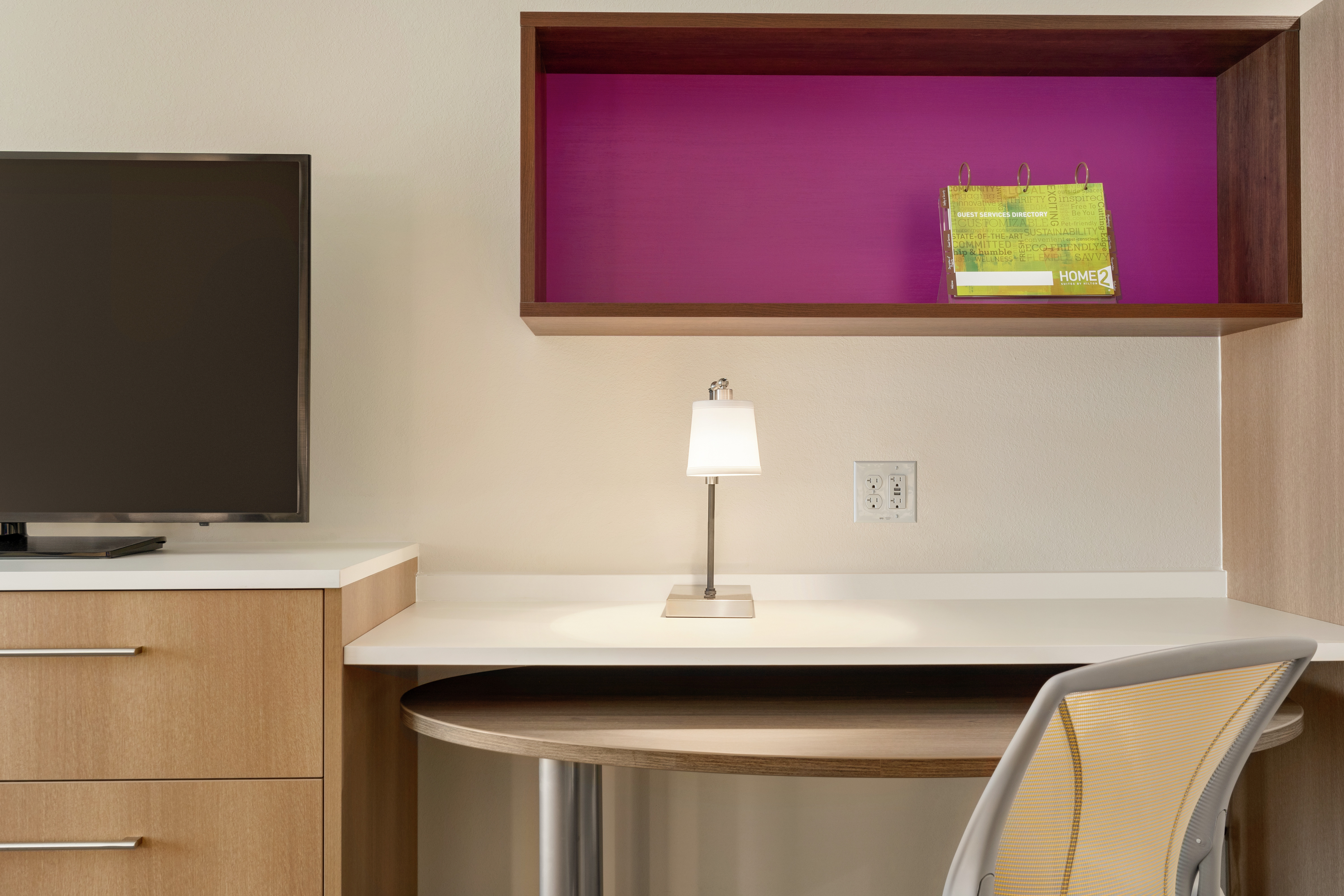 Studio suite work desk with ergonomic chair, built in shelving unit, and TV on top of dresser.