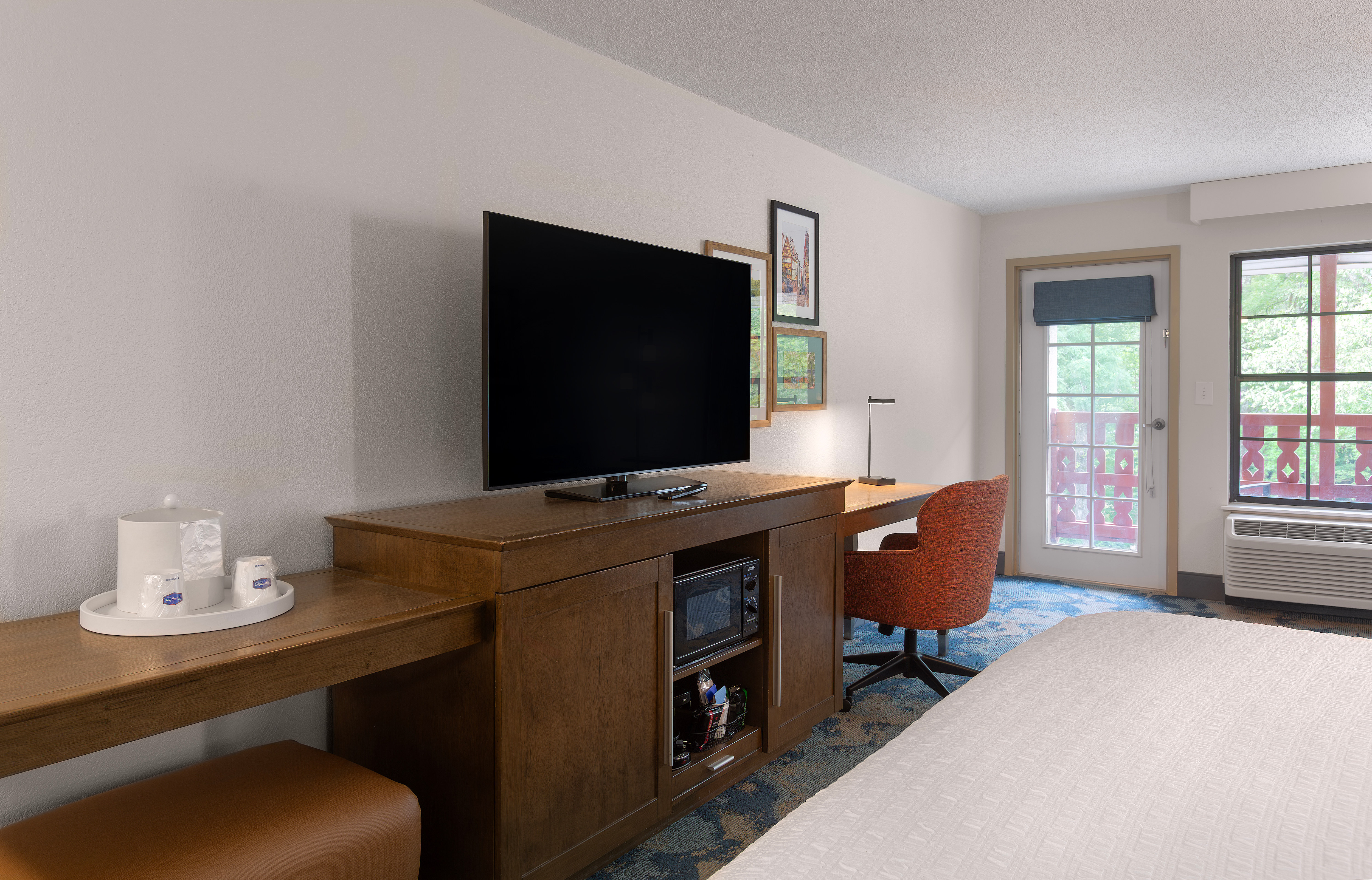 Television sitting on a television cabinet with a work desk and exterior door in a guest room