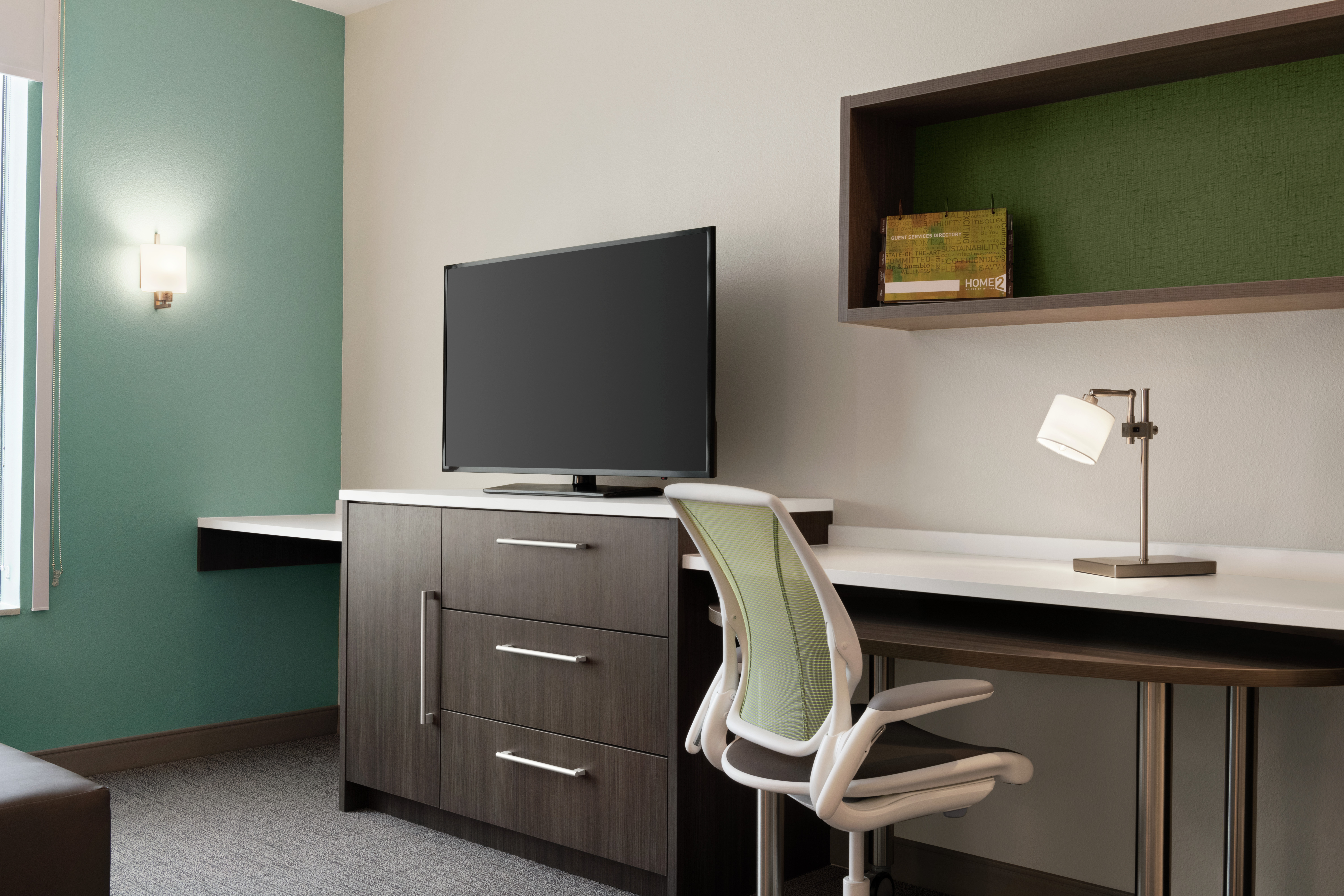Bright living area in suite featuring work desk with ergonomic chair and TV.