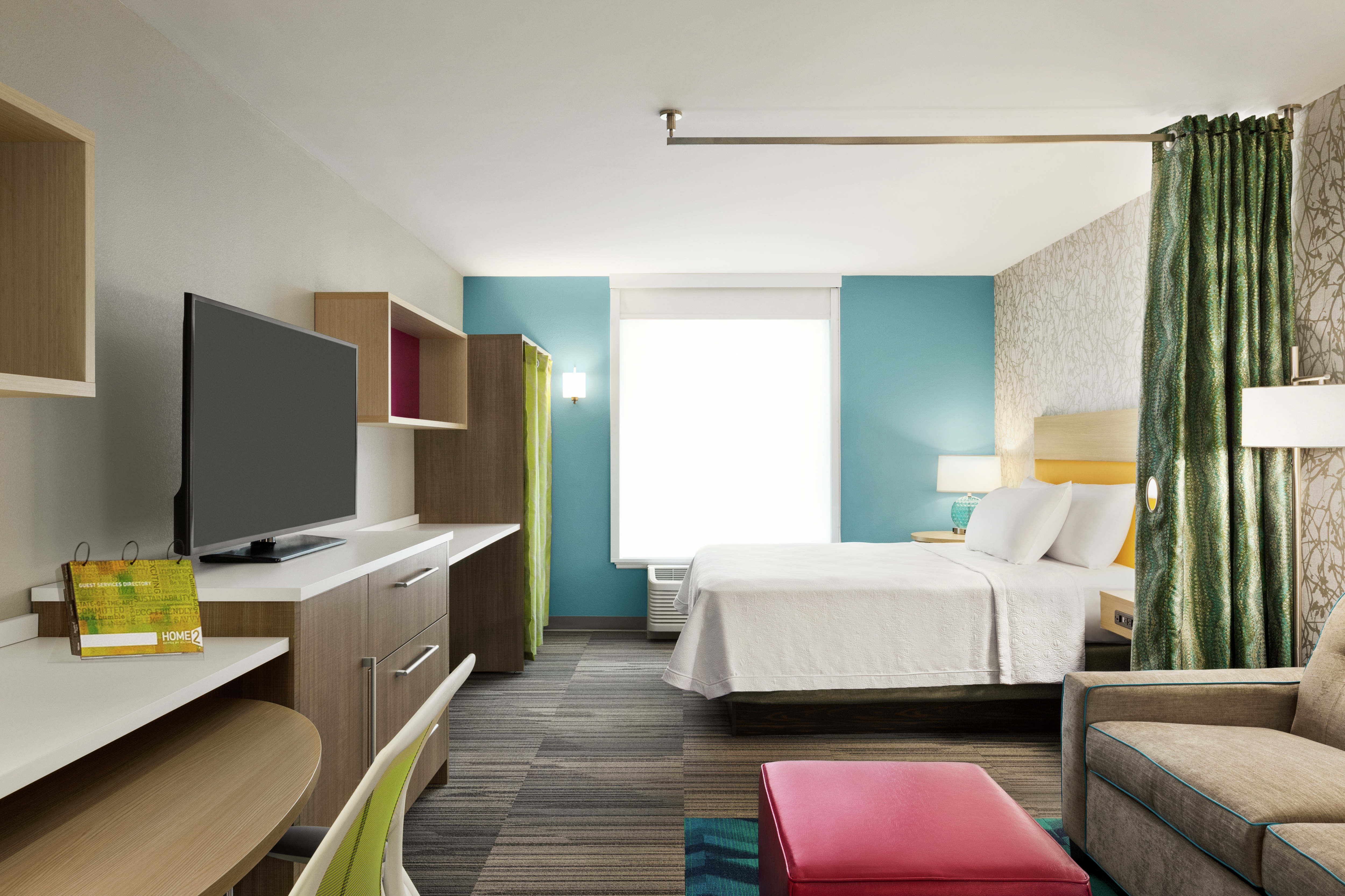 Spacious accessible studio suite featuring work desk with ergonomic chair, lounge area with sofa and TV, privacy curtain, and comfortable queen bed.