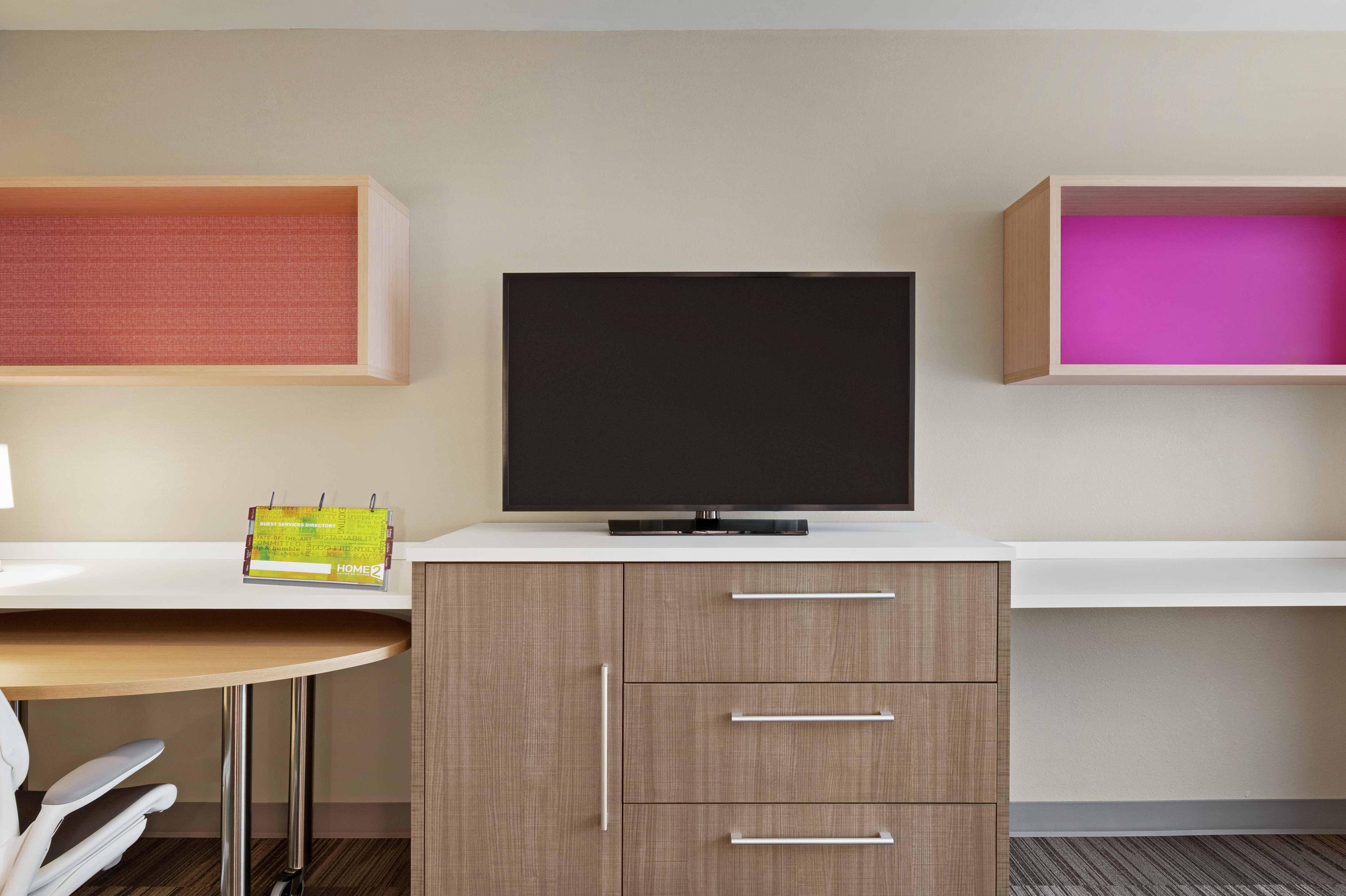 Bright accessible studio suite featuring work desk with ergonomic chair, built in storage, and TV.