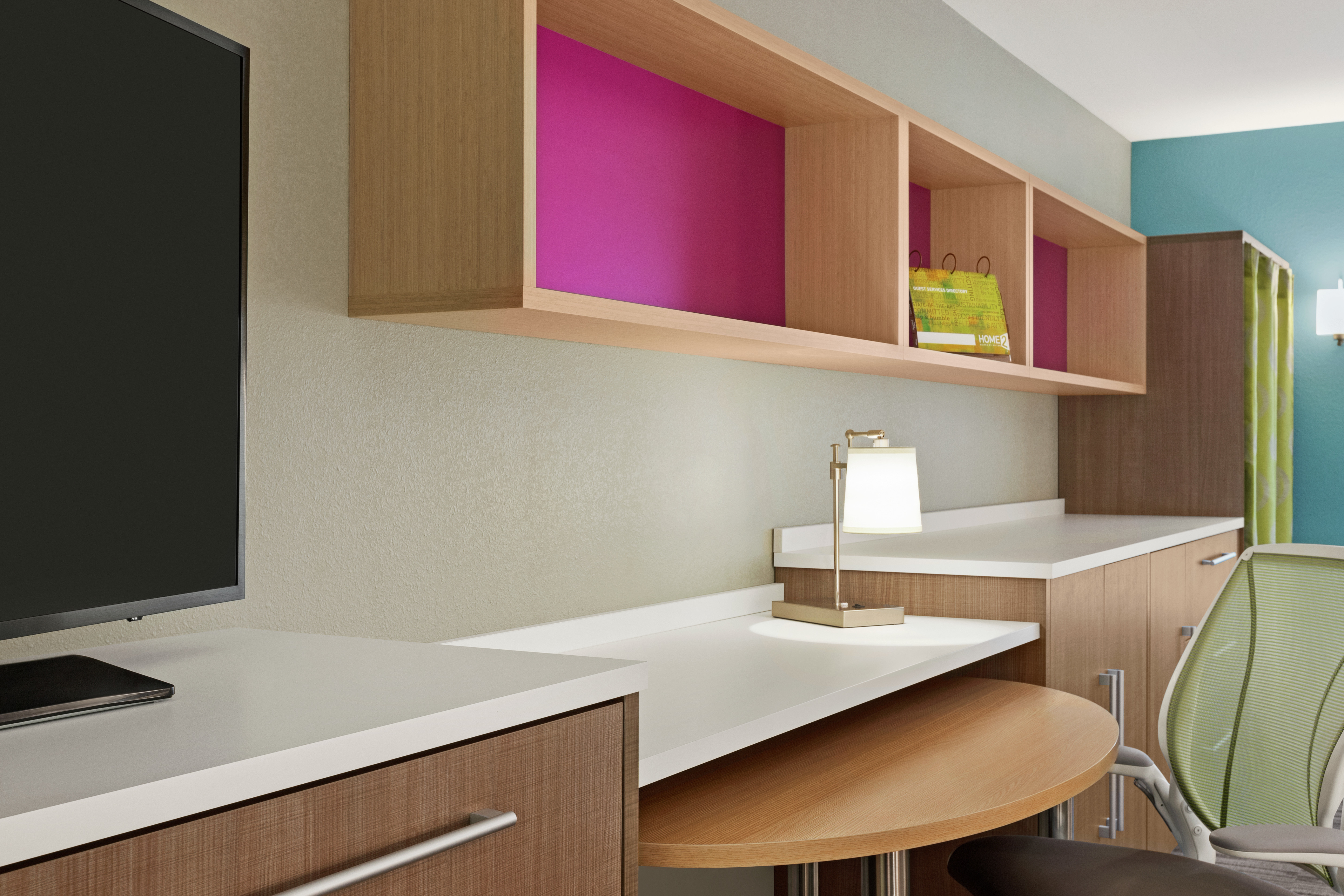 Bright studio suite featuring TV, work desk with ergonomic chair, and closet.