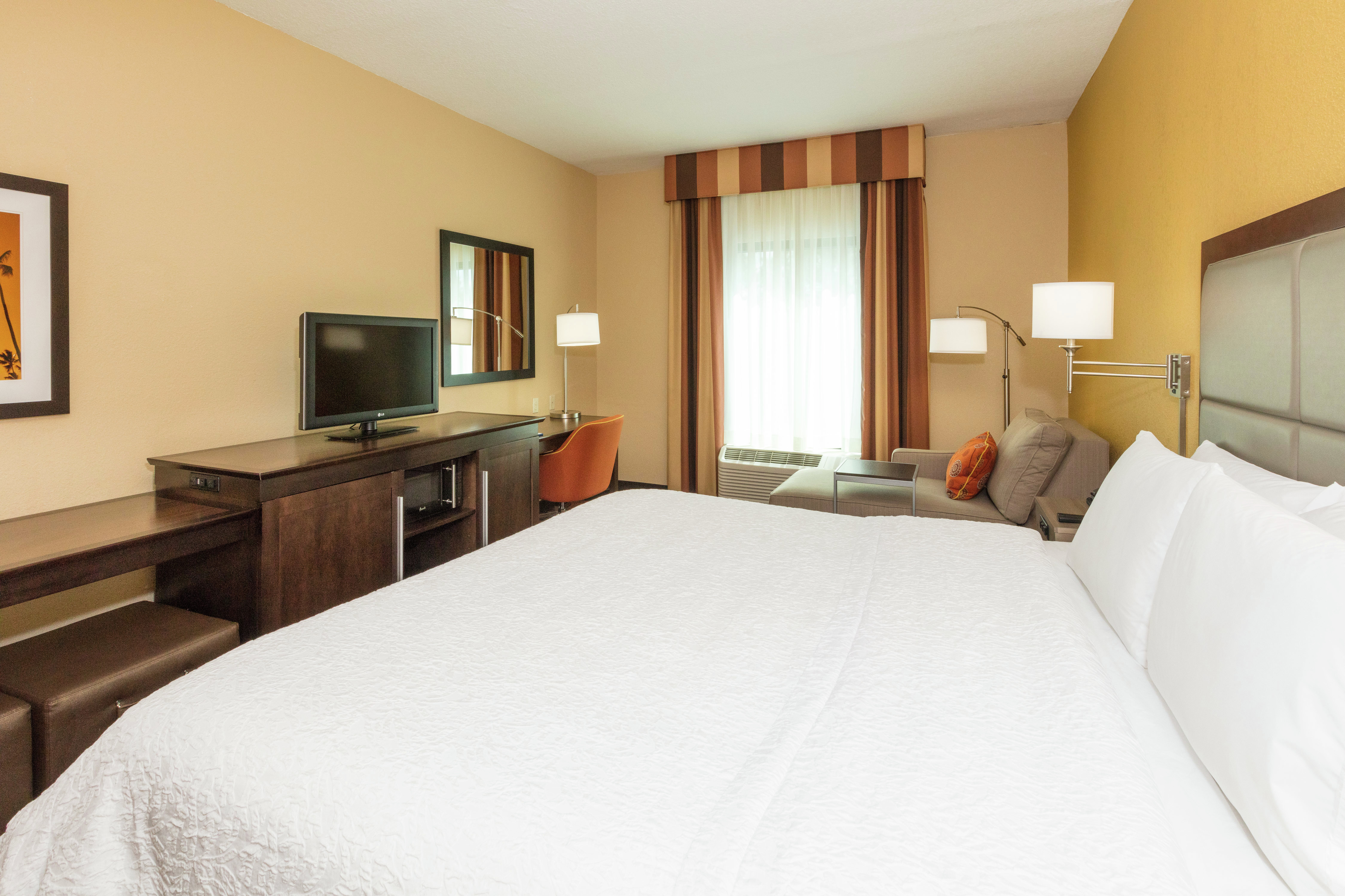 Guest Room With King Bed, Illuminated Lamps, TV, Work Desk, Window With Long Drapes, and Armchair