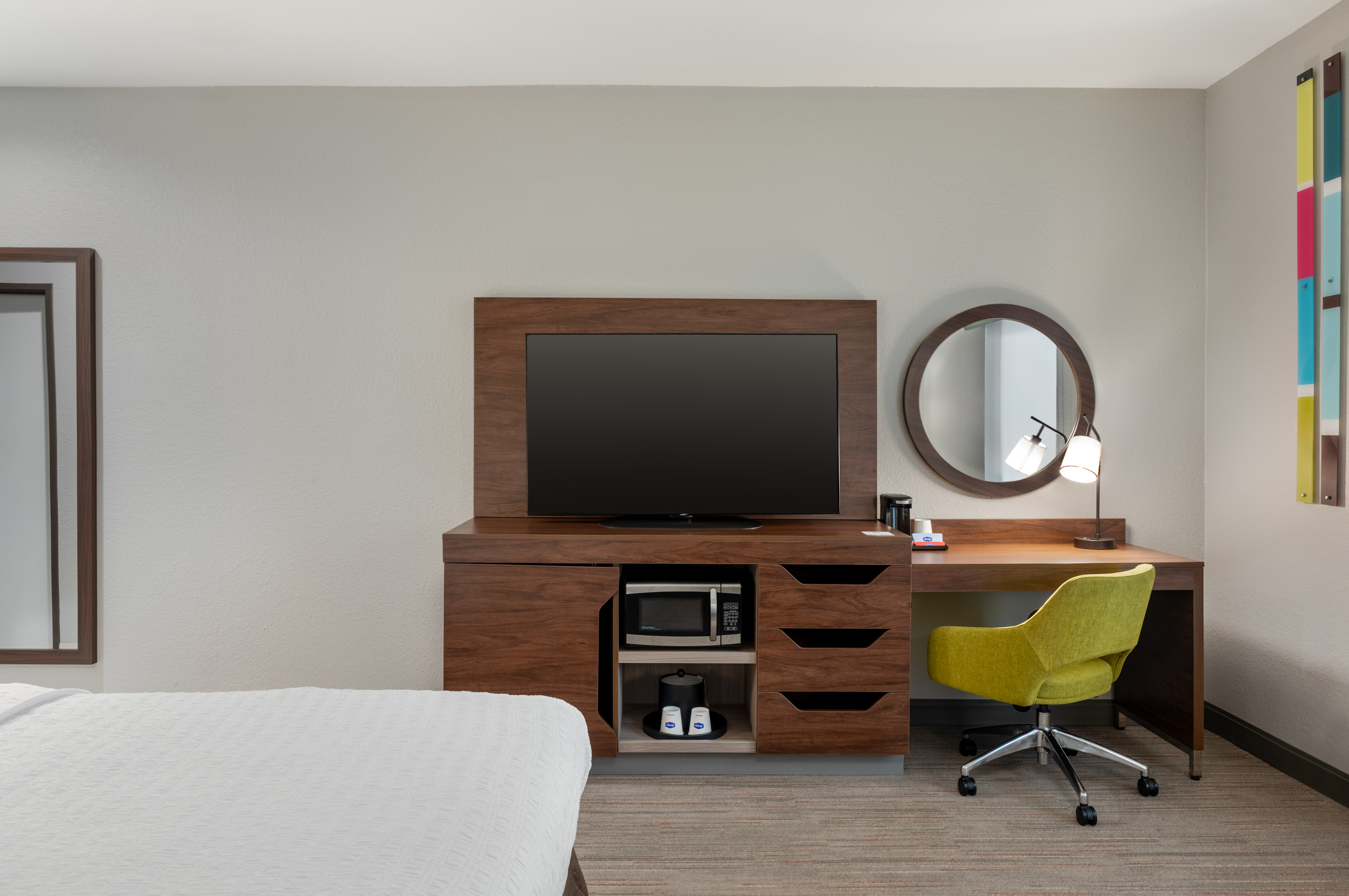 Guestroom work desk with a chair, next to the TV, and the end of one bed.
