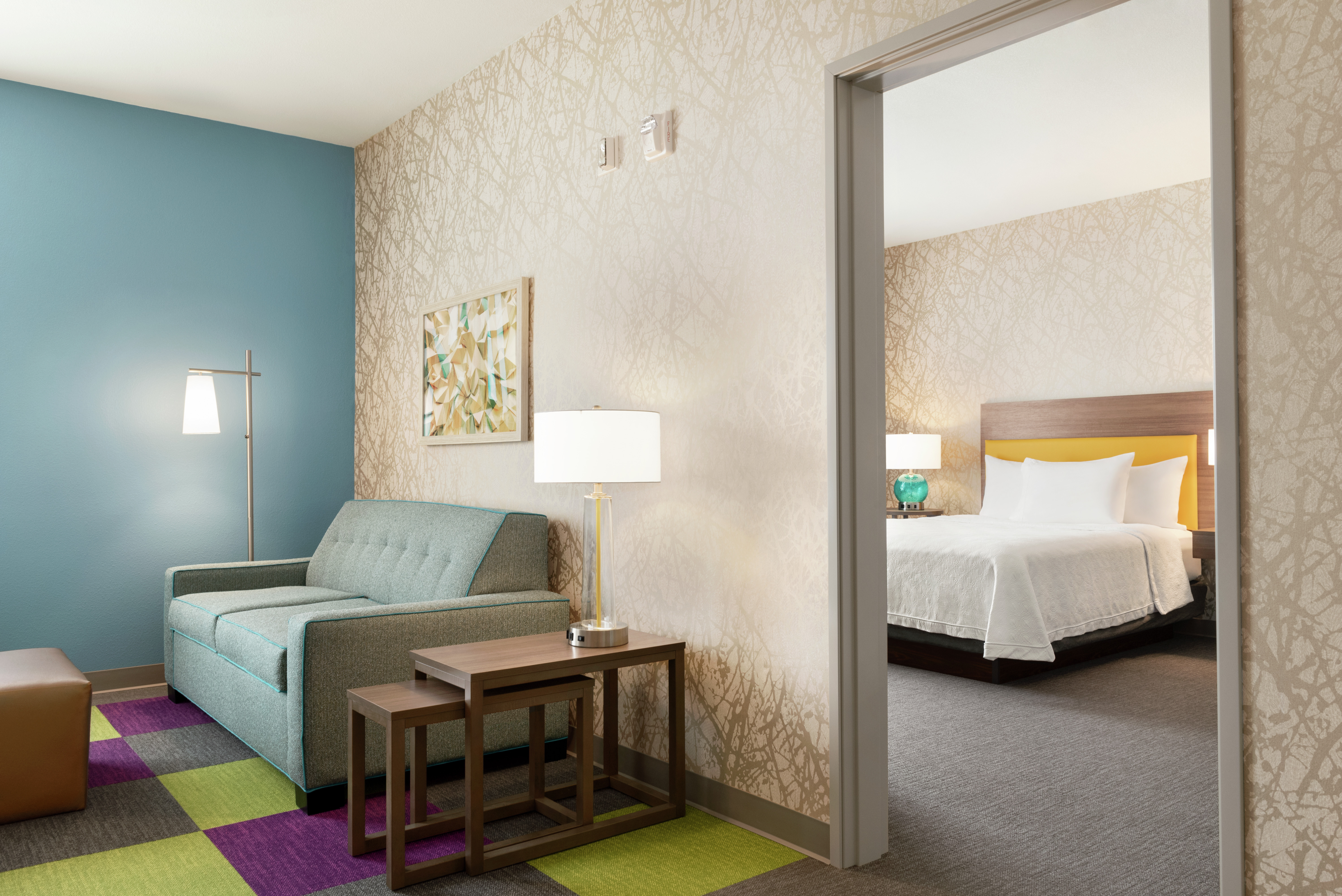 Spacious lounge area in suite with sofa and ottoman, and view into private bedroom with queen bed.