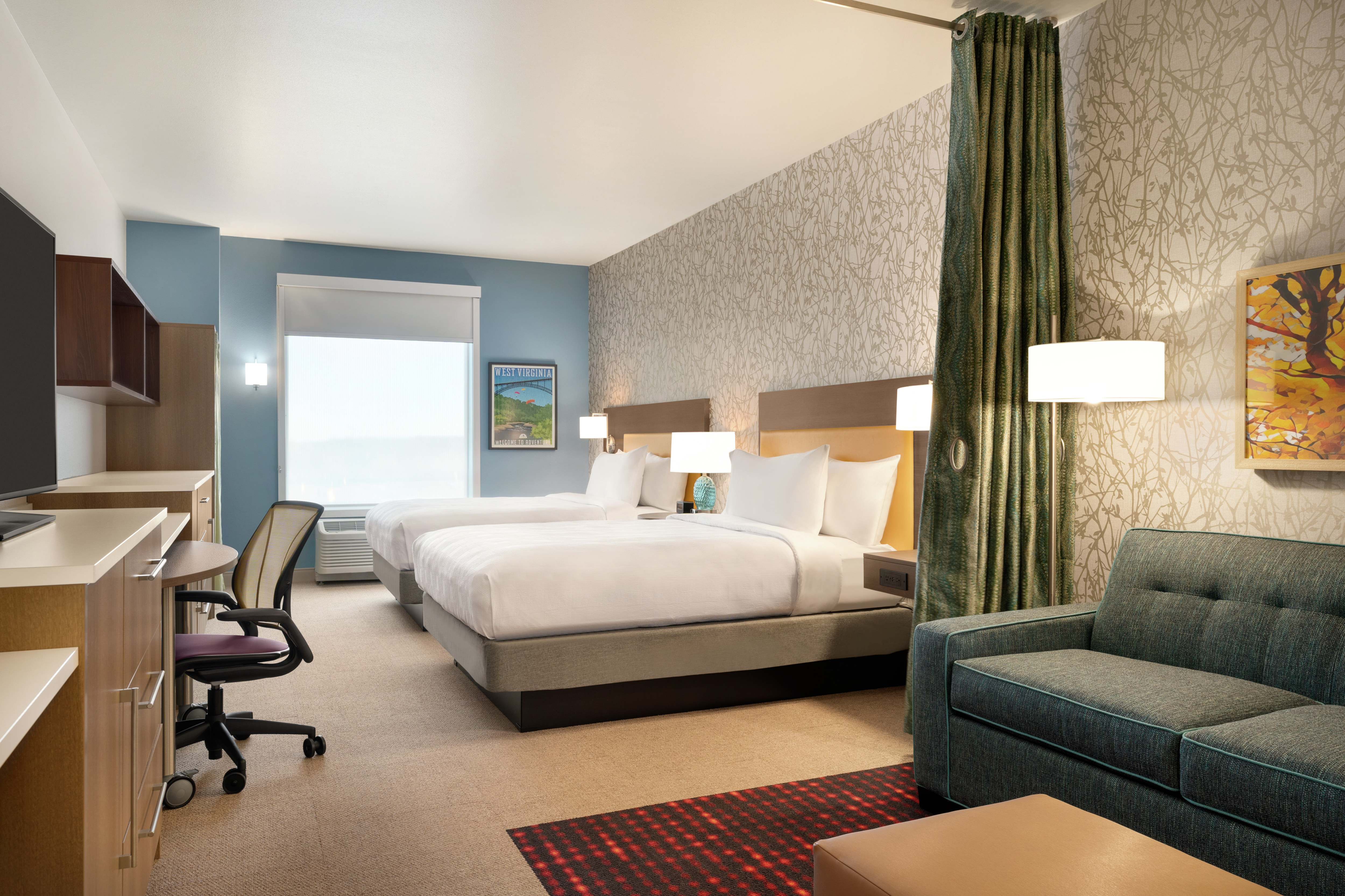 Bright studio suite featuring sofa, TV, work desk, and two comfortable queen beds.
