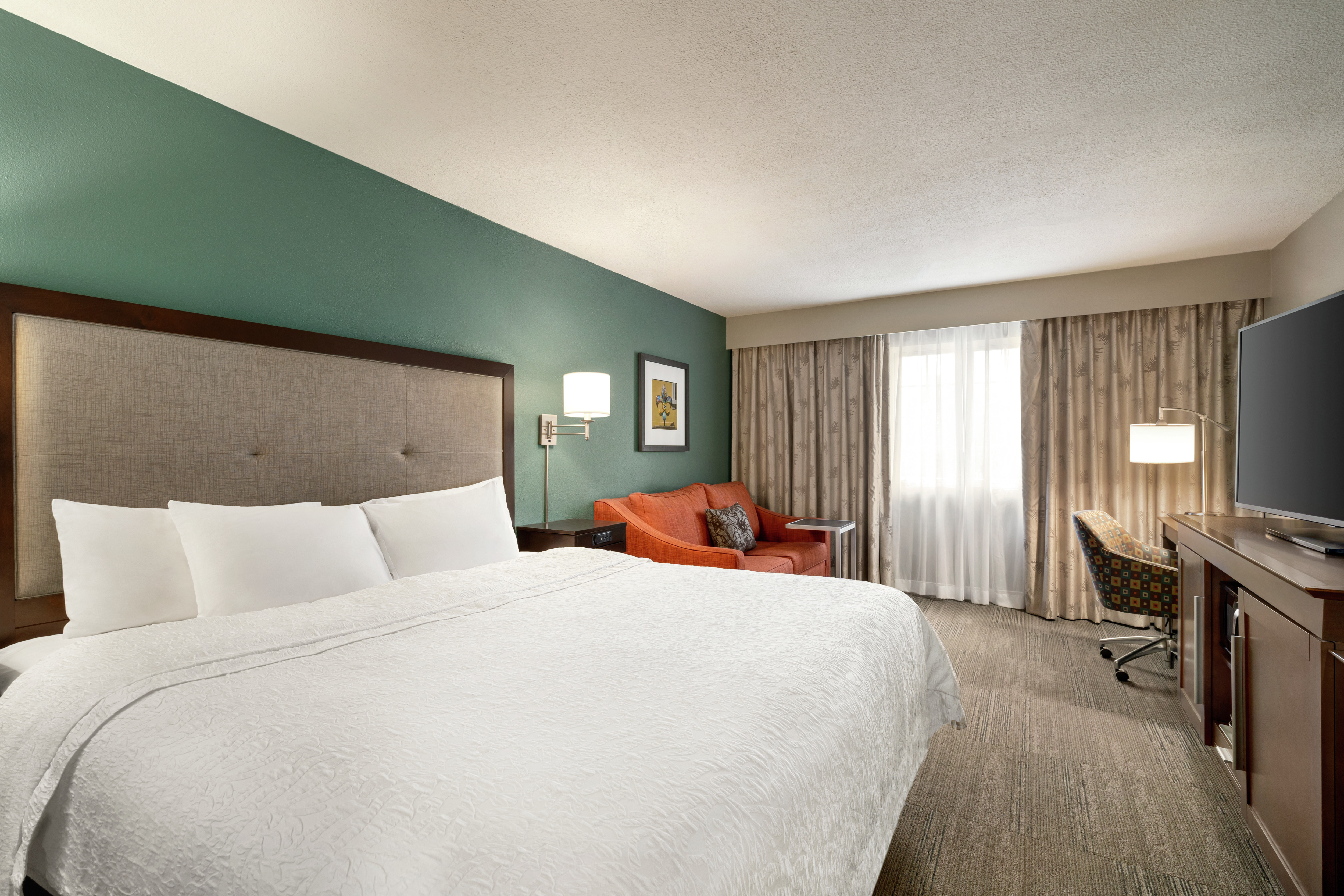 Spacious guest room featuring comfortable king bed, sofa, work desk, and TV.