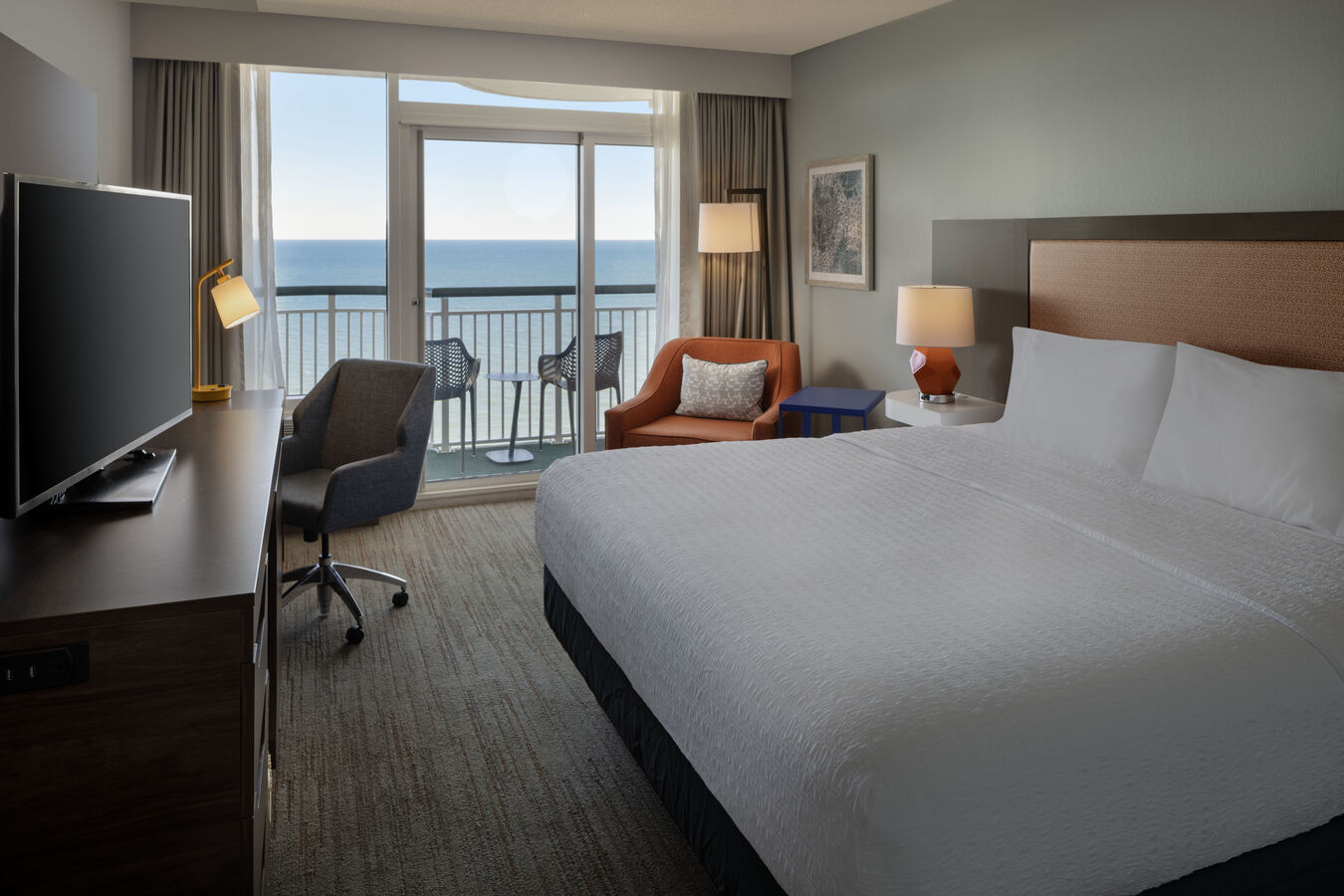 Hotel room with a king bed and wall of windows that includes a sliding door to the balcony with views of the ocean.