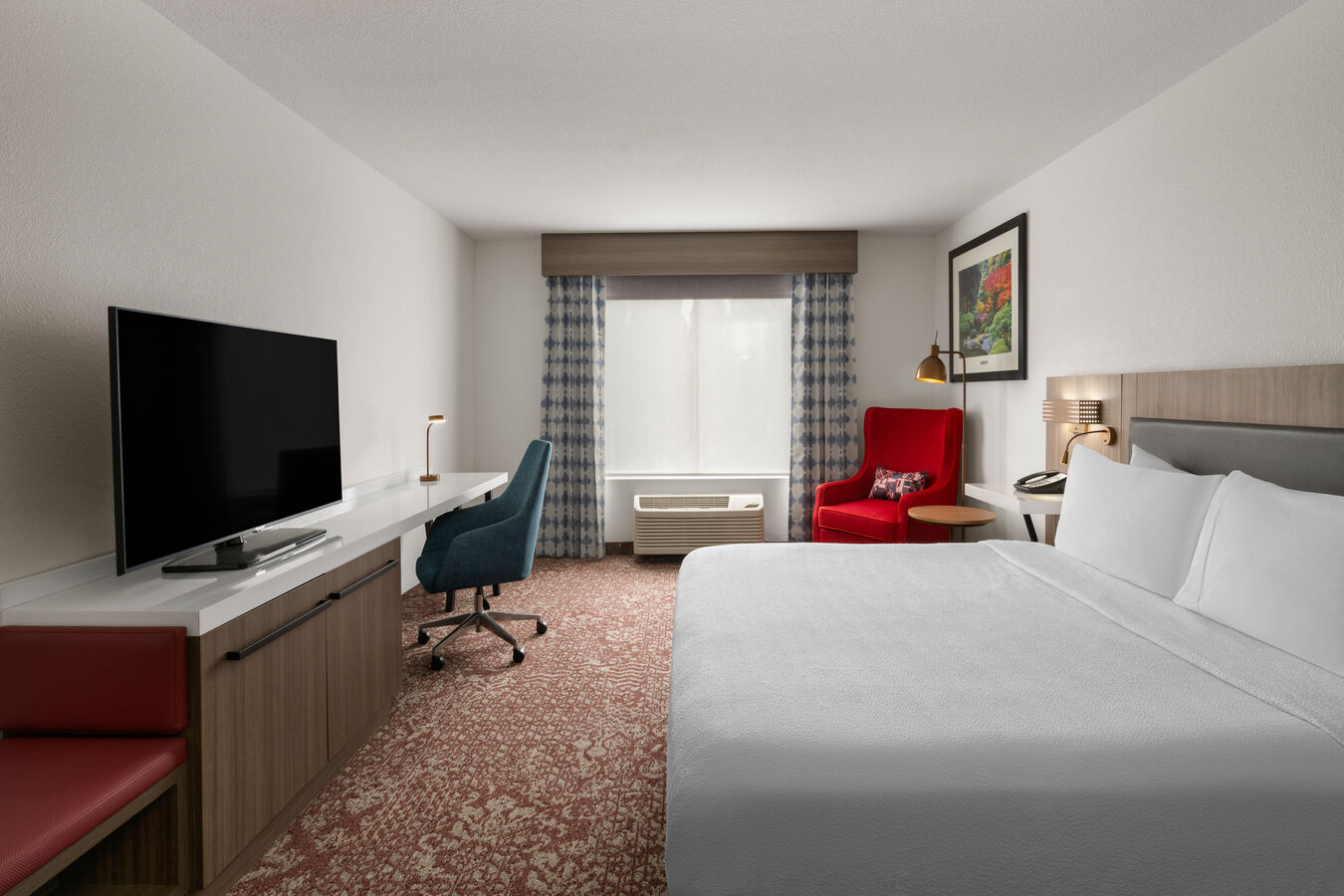 White bed with a television and a red chair