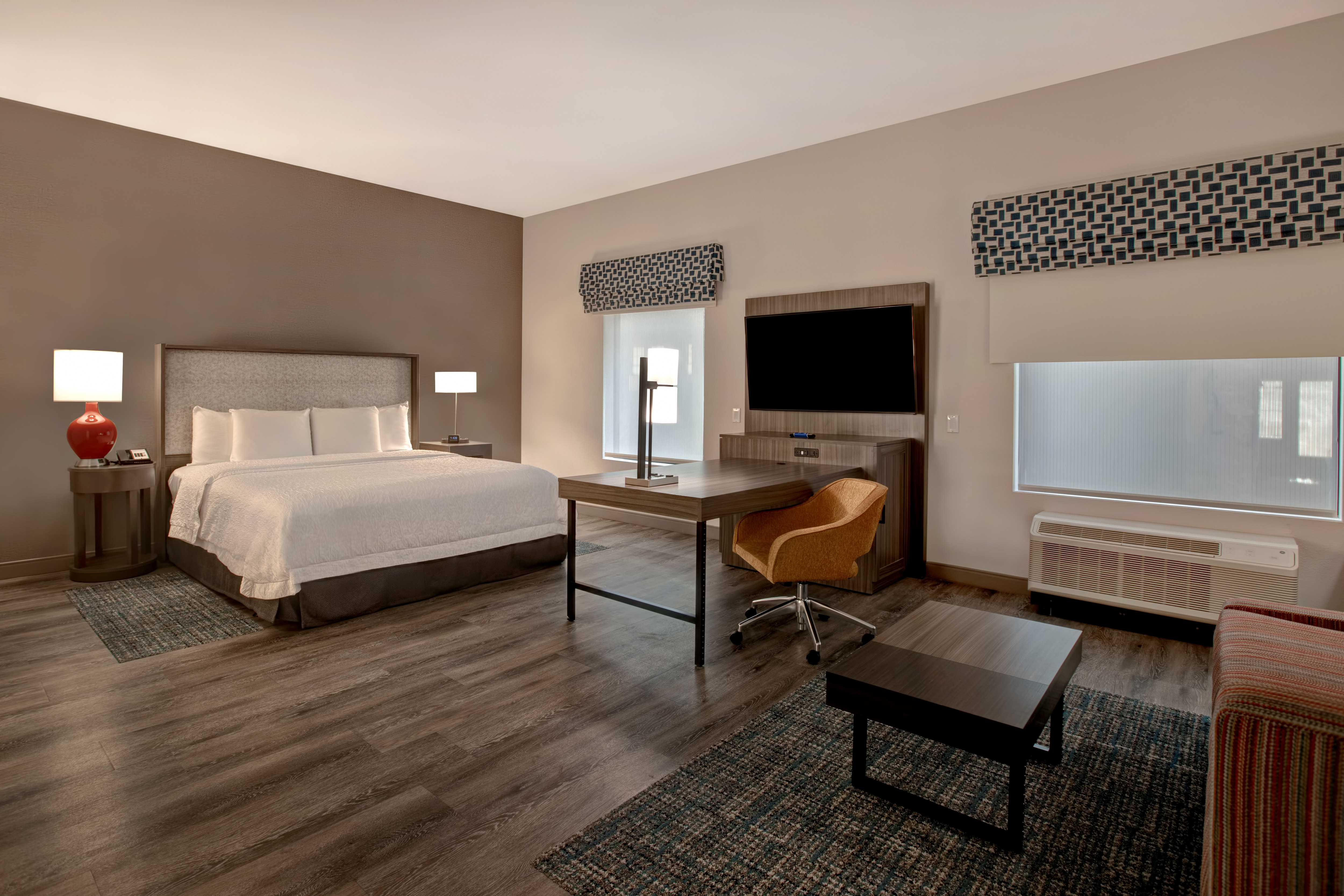 guest room with bed work desk television lounge area and window