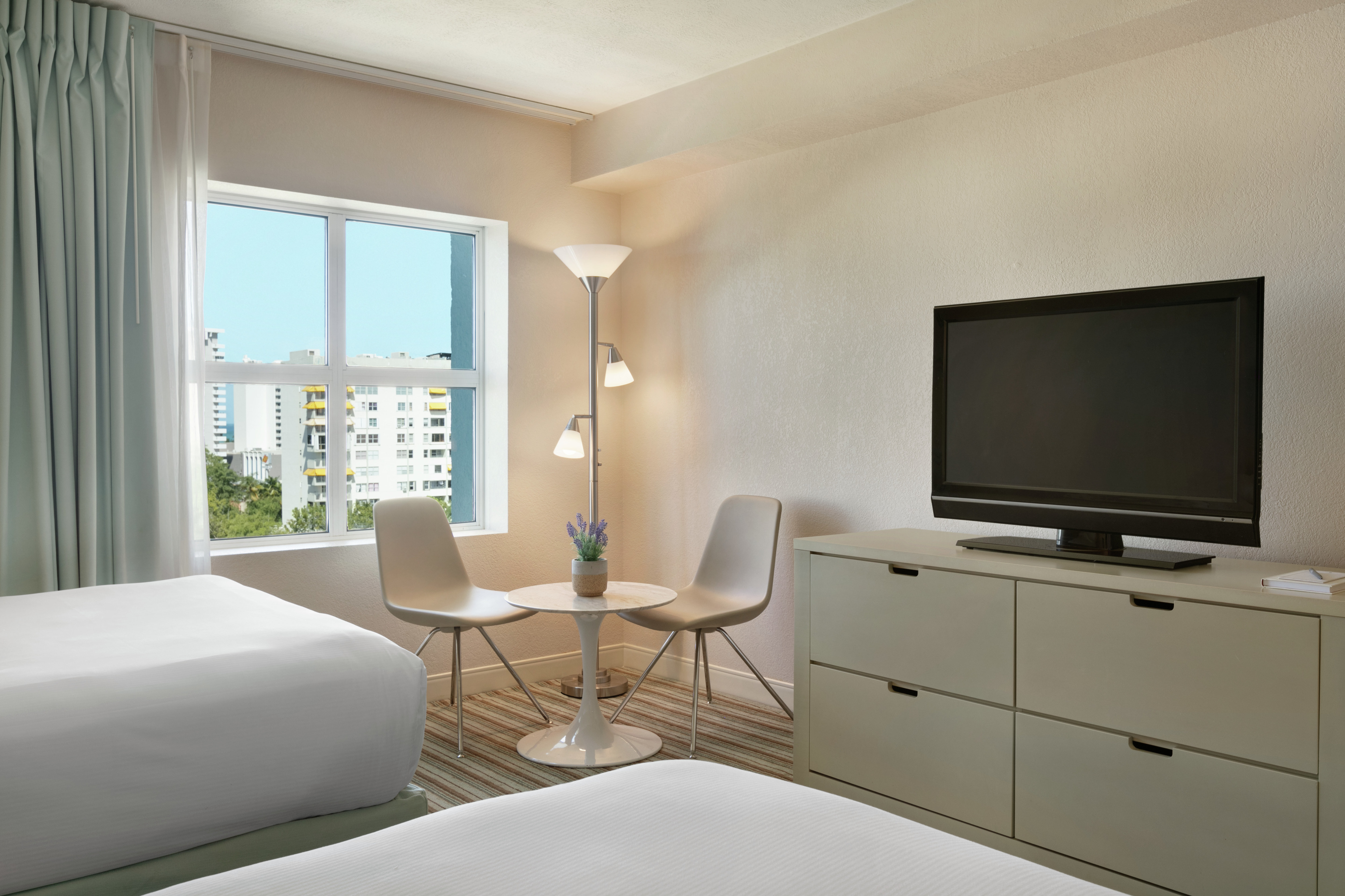 Bright studio featuring two comfortable double beds, TV, and seating area by the window with beautiful outside view.