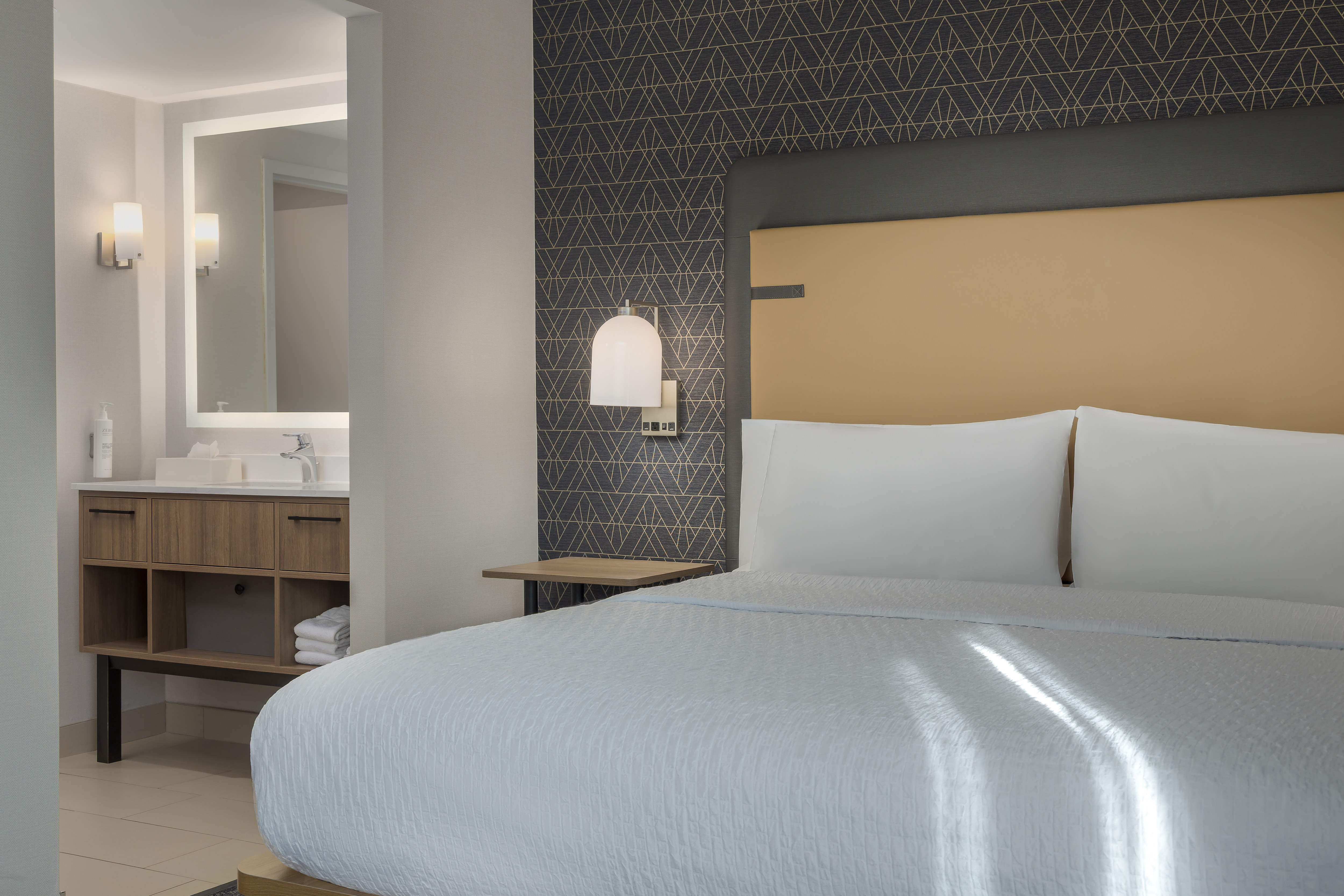 Bed in guest room with view through to vanity with mirror